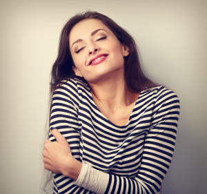 Happy young casual woman hugging herself.