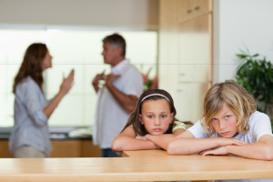 Sad looking siblings with their arguing parents behind them